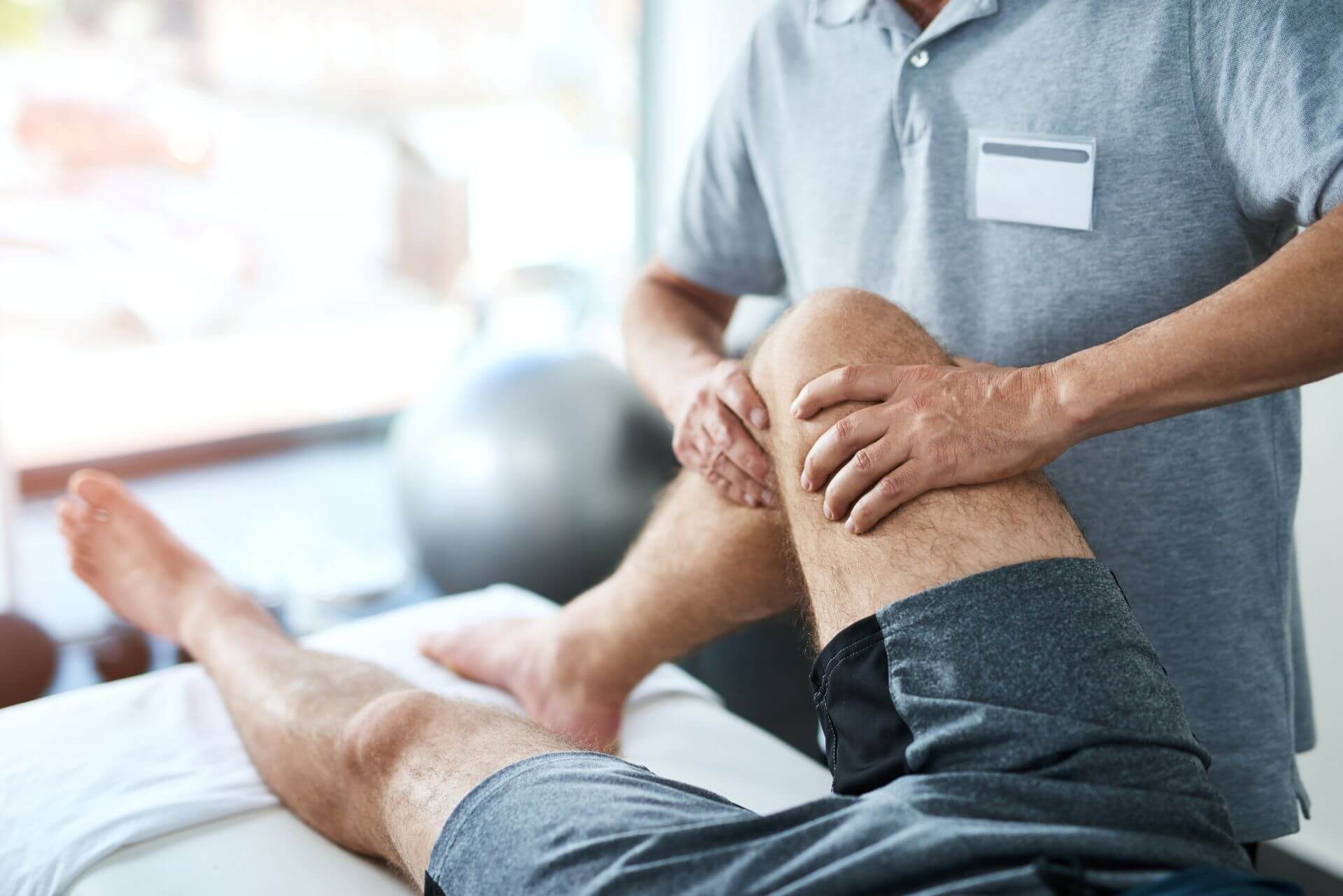 Fisioterapista che esegue una terapia manuale sul ginocchio di un paziente durante una seduta di riabilitazione