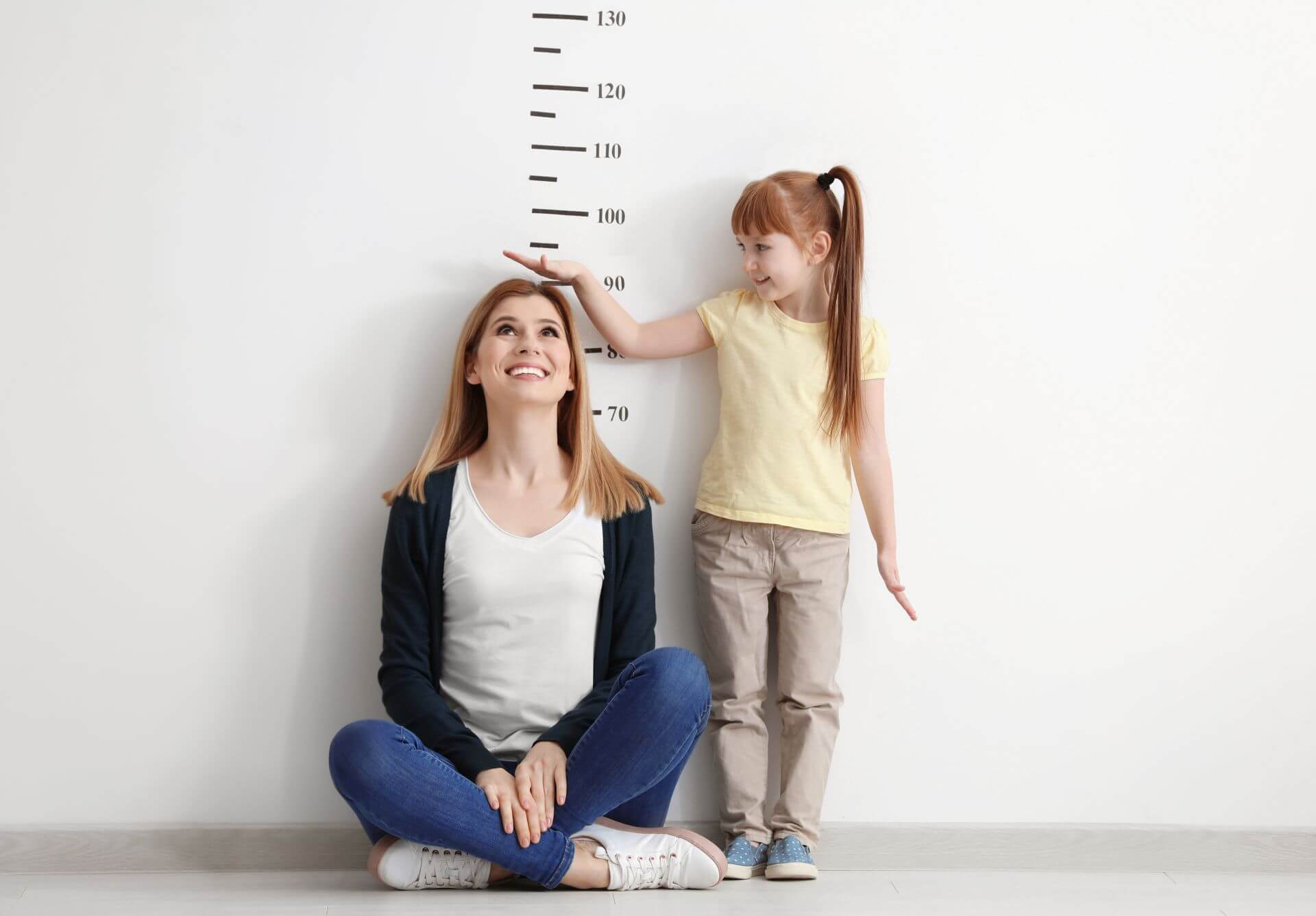Bambina che confronta la propria altezza con una donna davanti a un misuratore di crescita