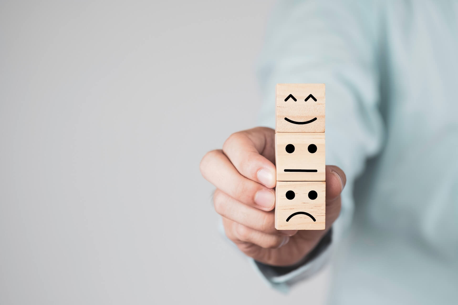 Persona che tiene tre blocchi di legno sovrapposti con espressioni felice, neutra e triste, rappresentando diversi stati emotivi e il benessere psicologico