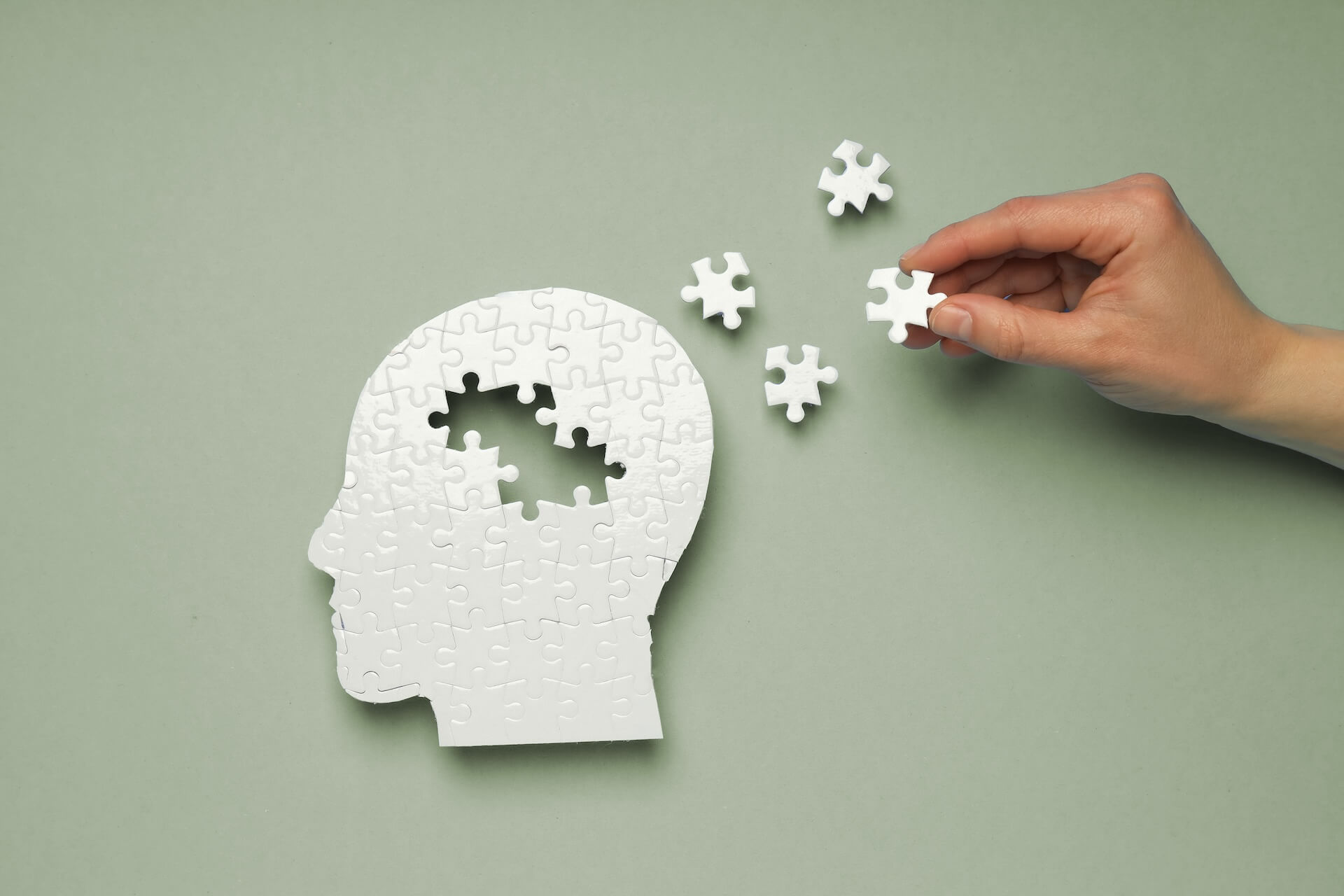 Mano che inserisce un pezzo di puzzle in una sagoma a forma di testa umana composta da tasselli, concetto di salute mentale, memoria e supporto cognitivo